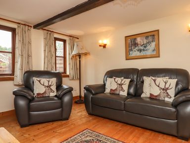 A living room with leather armchairs and sofa with deer cushions and framed picture at Northwood Barn in Okehampton