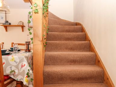 A carpeted staircase next to a dining table with a tablecloth and wooden chairs at Northwood Barn in Okehampton