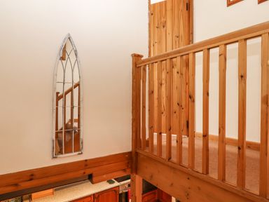 A wooden staircase railing and a door with a tall narrow mirror on the wall above a kitchen area at Northwood Barn in Okehampton