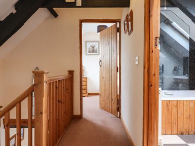 A hallway with wooden railing and doors leading to a room and a bathroom at Northwood Barn in Okehampton