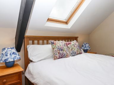 A bedroom with a wooden bed under a skylight with floral pillows and blue patterned lamps on wooden nightstands at Northwood Barn in Okehampton