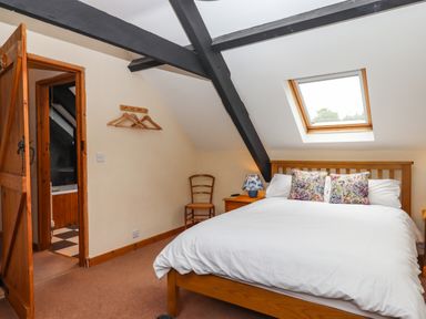 A bedroom with a wooden bed a chair and a nightstand with a lamp at Northwood Barn in Okehampton