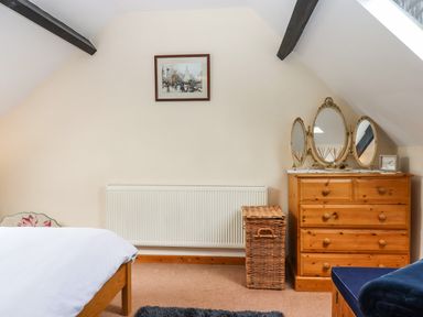 A bedroom with wooden dresser and wicker basket under sloped ceiling at Northwood Barn in Okehampton
