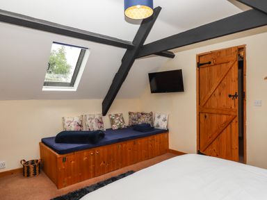 A bedroom with a wooden storage bench under a skylight window and a wall-mounted TV at Northwood Barn in Okehampton