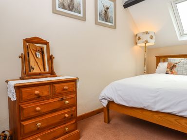 A bedroom with a wooden chest of drawers a mirror a bed with white bedding a cushion with an animal print and a floor lamp at Northwood Barn Okehampton