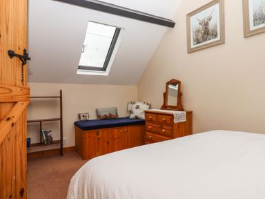 A bedroom with a bed white bedding wooden dresser with mirror skylight window and cushioned bench at Northwood Barn in Okehampton