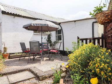 An outdoor patio area with a table and chairs under an umbrella and yellow flowers at Northwood Barn in Okehampton