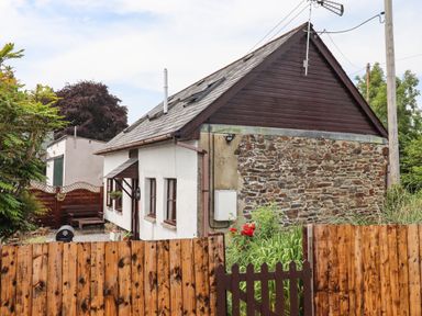 A small house with stone and plaster walls a wooden fence and garden at Northwood Barn in Okehampton
