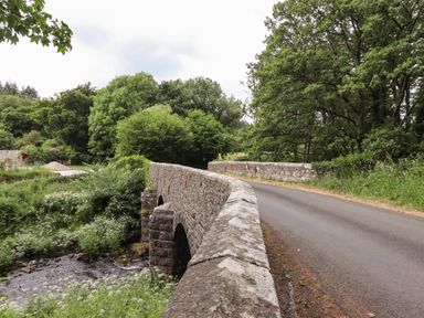 A stone bridge over a river surrounded by trees and greenery at Northwood Barn in Okehampton