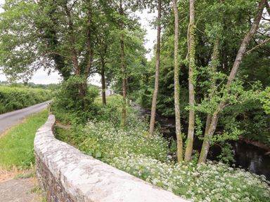 A country road beside a stone wall with trees and a river at Northwood Barn in Okehampton