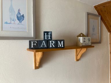 A wooden wall shelf with blocks spelling farm and a calendar showing March 29 with framed bird pictures on the wall at Northwood Barn in Okehampton