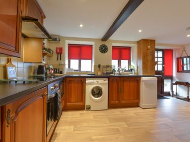 A kitchen with wooden cabinets washing machine dishwasher and red window blinds at Northwood Barn in Okehampton