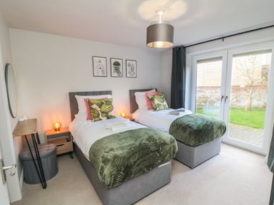 A bedroom with two single beds side by side with green blankets and pillows near glass doors at The Annexe in Bridlington