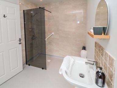 A bathroom with a glass shower screen a sink with a faucet and soap dispenser and a round mirror at The Annexe in Bridlington