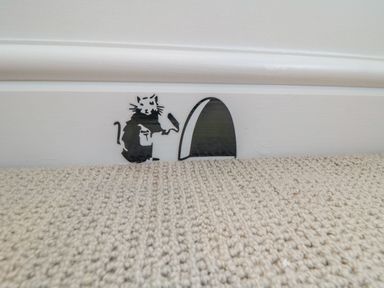 A small wall decal of a rat painting a mouse hole on a white baseboard above a beige carpet at The Annexe in Bridlington