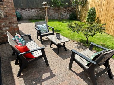 A garden patio with outdoor seating including a bench and chairs around a small table with cushions on the seats at The Annexe in Bridlington