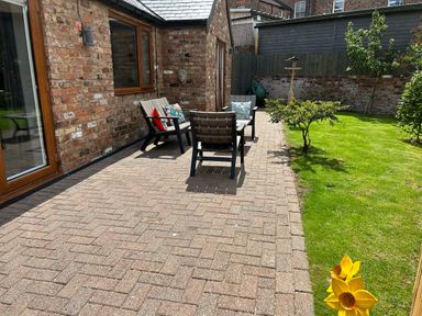 A brick patio with outdoor chairs and cushions next to a brick house and a grassy garden at The Annexe in Bridlington