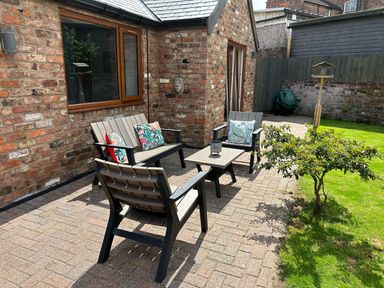 An outdoor patio with chairs a table and cushions next to a brick house and a small tree at The Annexe in Bridlington