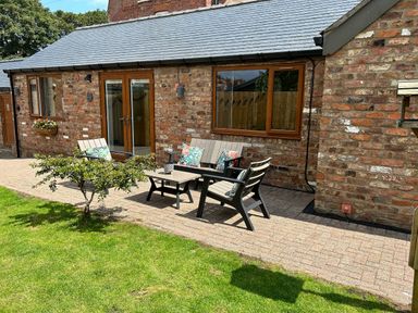An outdoor seating area with chairs, a bench, and a table on a paved patio next to a brick building with windows and a door at The Annexe in Bridlington