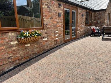 An outdoor patio area with brick walls wooden framed windows and doors a planter with flowers and patio furniture at The Annexe in Bridlington