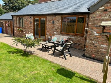 A patio area with outdoor chairs, a table, cushions, and a small tree on a grass lawn at The Annexe in Bridlington
