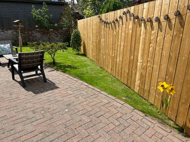 A backyard with a wooden fence string lights two chairs a small table green grass and yellow flowers at The Annexe in Bridlington