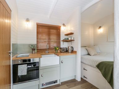 A small kitchen with an oven sink countertop toaster kettle and a bed with pillows and a blanket in a compact living space at Willow in Kemble
