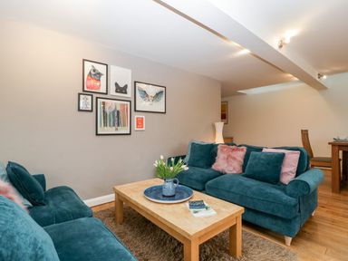 A living room with teal sofas a wooden coffee table flowers on the table and framed pictures on the wall at Owl Barn Marston Stannett near Leominster