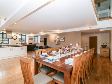 A dining area with a long wooden table set with dishes and glasses next to a kitchen and sitting area at Owl Barn Marston Stannett near Leominster