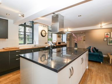 A kitchen with a large island counter black countertop utensils and a vase with flowers and a living area with a blue sofa and framed pictures at Owl Barn Marston Stannett near Leominster