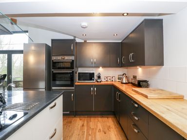 A kitchen with dark cabinets wooden countertops stainless steel appliances and a wooden floor at Owl Barn in Marston Stannett near Leominster