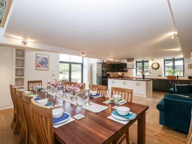 A dining area with a long wooden table set for ten beside an open kitchen and sitting area at Owl Barn in Marston Stannett near Leominster