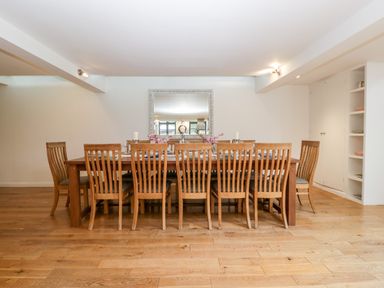 A dining room with a long wooden table and twelve wooden chairs and a large mirror on the wall at Owl Barn in Marston Stannett near Leominster