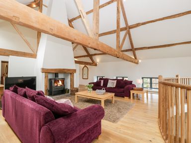 A living room with purple sofas a fireplace wooden beams and a coffee table at Owl Barn Marston Stannett near Leominster