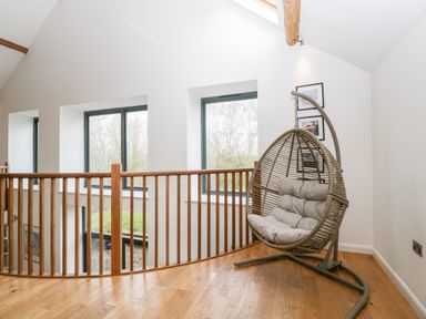 An upstairs area with wooden flooring railing and a hanging wicker chair with cushions at Owl Barn in Marston Stannett near Leominster