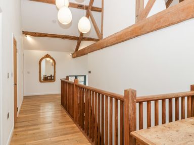 A hallway with wooden floor wooden railing ceiling beams and a wall mirror at Owl Barn Marston Stannett near Leominster