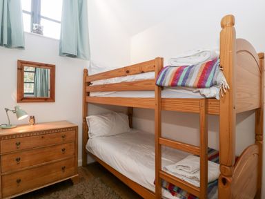 A bedroom with wooden bunk beds a wooden dresser with a lamp and mirror at Owl Barn in Marston Stannett near Leominster