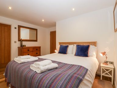 A bedroom with a bed with folded towels on a striped blanket two blue pillows a wooden dresser a mirror and two wooden doors at Owl Barn Marston Stannett near Leominster