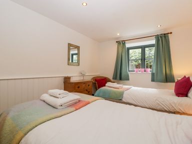 A bedroom with two single beds a wooden chest of drawers a mirror a window with curtains and towels on the beds at Owl Barn in Marston Stannett near Leominster