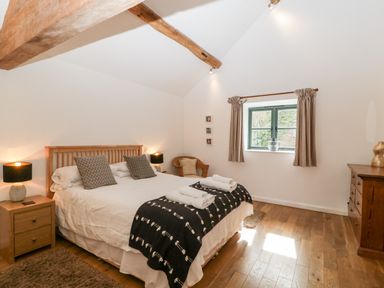 A bedroom with a large bed bedside tables with lamps a wooden dresser a window with curtains and exposed wooden beams at Owl Barn Marston Stannett near Leominster