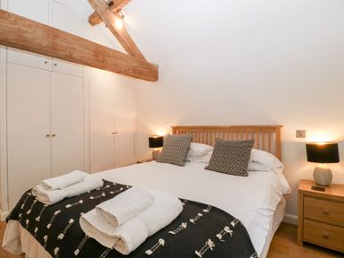 A bedroom with a wooden bed with white linens and black patterned pillows two bedside tables with lamps and built in wardrobes at Owl Barn Marston Stannett near Leominster