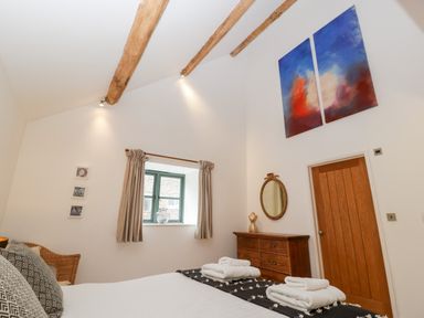 A bedroom with wooden beams on ceiling a wooden dresser and door a window with curtains and two pieces of abstract art on the wall at Owl Barn Marston Stannett near Leominster