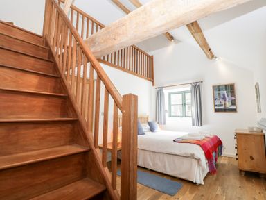 A bedroom with a wooden staircase white bed and window at Owl Barn Marston Stannett near Leominster