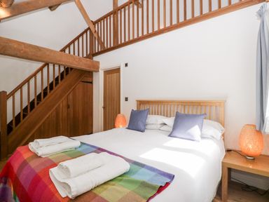 A bedroom with a double bed with white bedding and blue pillows next to wooden staircase and bedside tables with lamps at Owl Barn Marston Stannett near Leominster