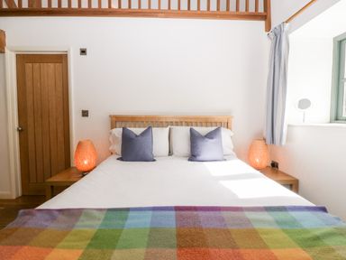 A bedroom with a wooden bed frame two bedside tables with lamps and a window at Owl Barn in Marston Stannett near Leominster