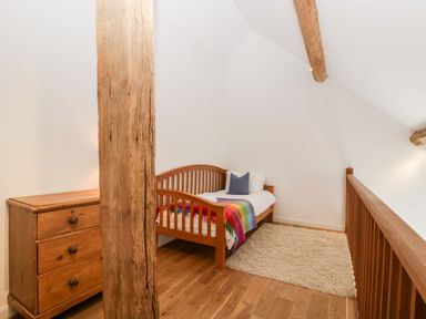 A bedroom with a single wooden bed a wooden chest of drawers and a rug at Owl Barn in Marston Stannett near Leominster