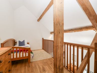 A loft bedroom with a wooden bed a dresser exposed wooden beams and a beige rug at Owl Barn Marston Stannett near Leominster