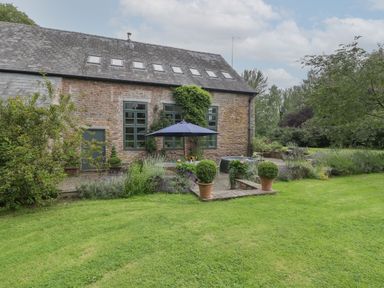 A stone house with multiple windows and skylights surrounded by a garden with trimmed grass and outdoor seating at Owl Barn Marston Stannett near Leominster
