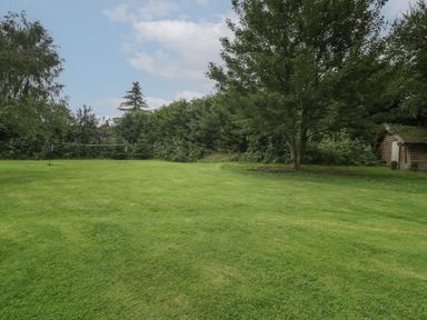 A grassy garden with a badminton net a tree and a wooden shed at Owl Barn in Marston Stannett near Leominster