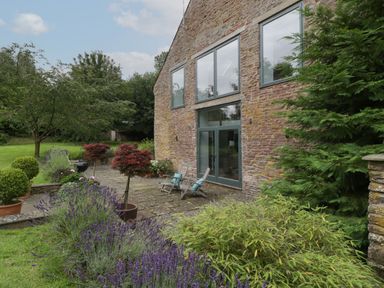 A garden area with potted plants, two chairs on a stone patio next to a stone house with large windows at Owl Barn in Marston Stannett near Leominster